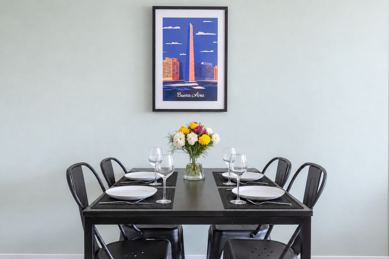 A dining table set for four with a framed cityscape poster above it.
