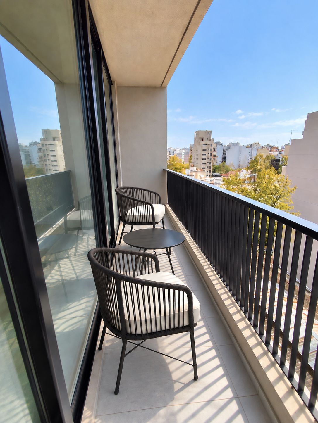 Un balcón con dos sillas y una mesa, con vista a un paisaje urbano.