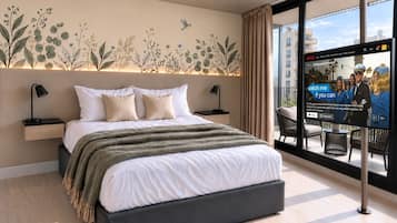 A modern hotel room with a large bed, a wall-mounted TV, and a balcony with a view of the city.