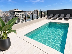 Une piscine sur le toit, avec une eau d’un bleu cristallin, entourée de chaises longues et agrémentée d’une plante en pot.