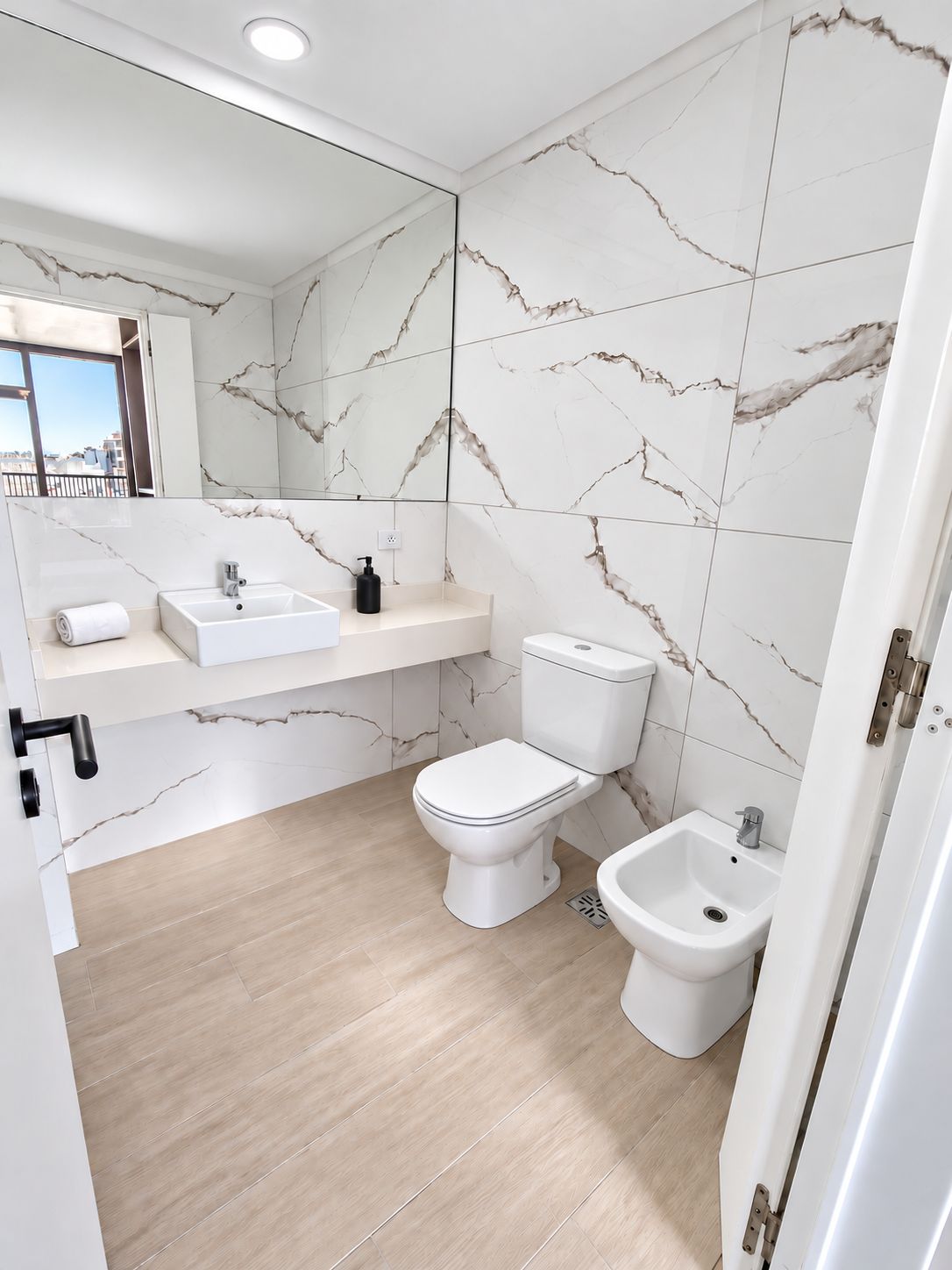 A modern bathroom with a marble backsplash, a white sink, a toilet, and a bidet.