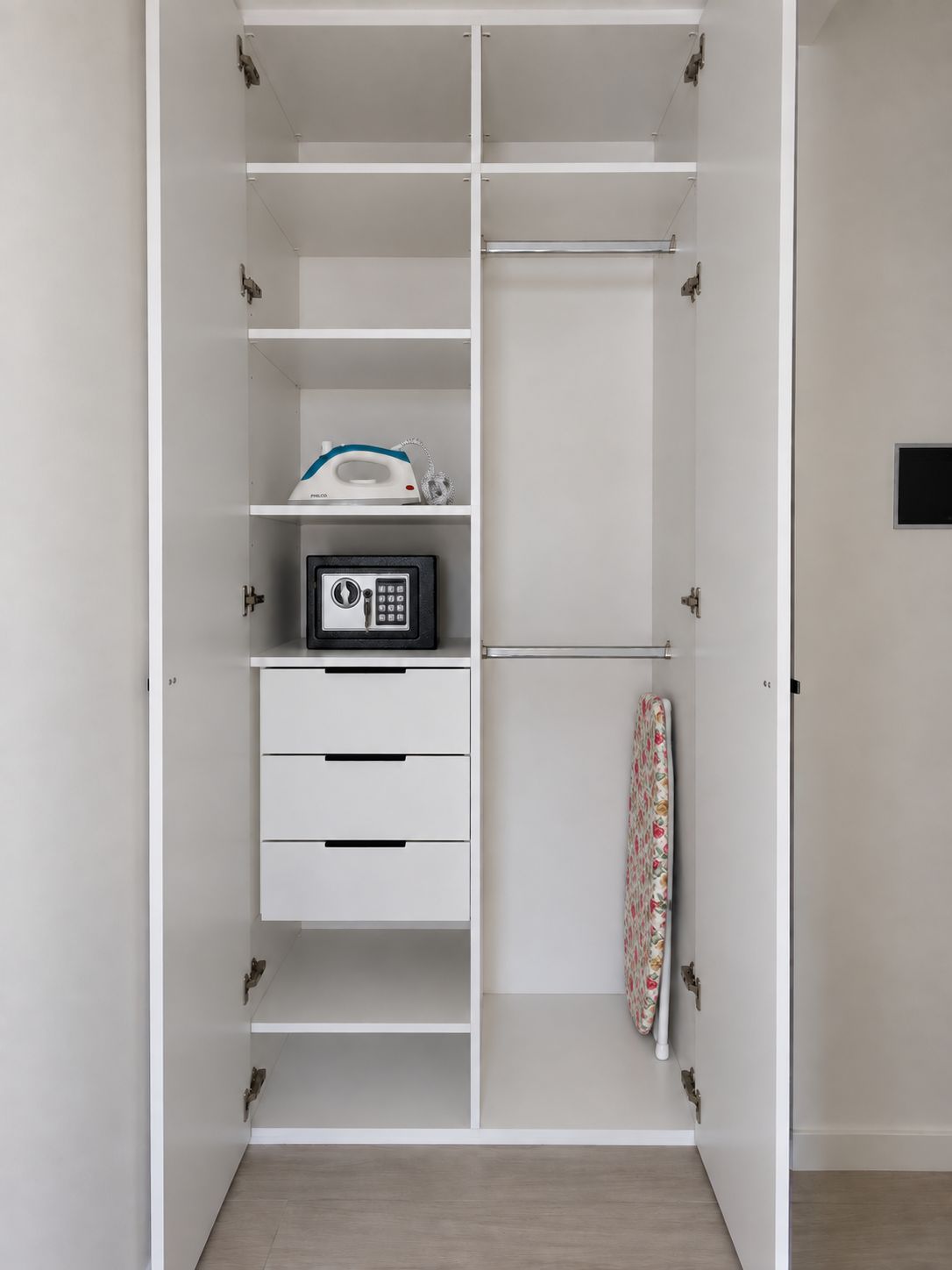 A white wardrobe with multiple compartments, including a hanging rod, a microwave, and a small ironing board.