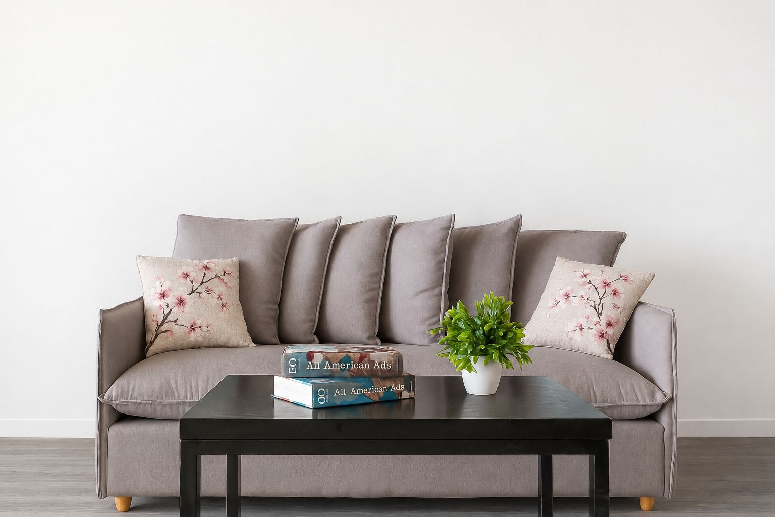 A grey sofa with floral cushions, a black coffee table, and a potted plant.
