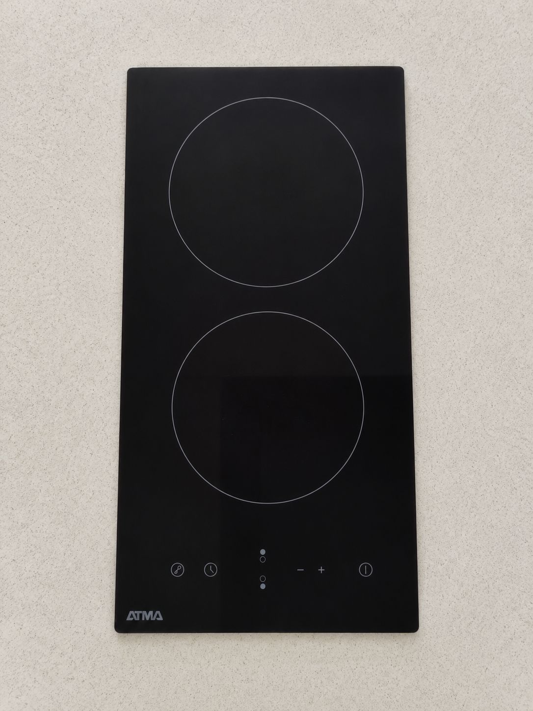 A black ATMA induction cooktop with two circular cooking surfaces and control buttons.