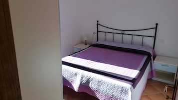 Una cama individual con cabecera, una mesita de noche con lámpara y un velador.