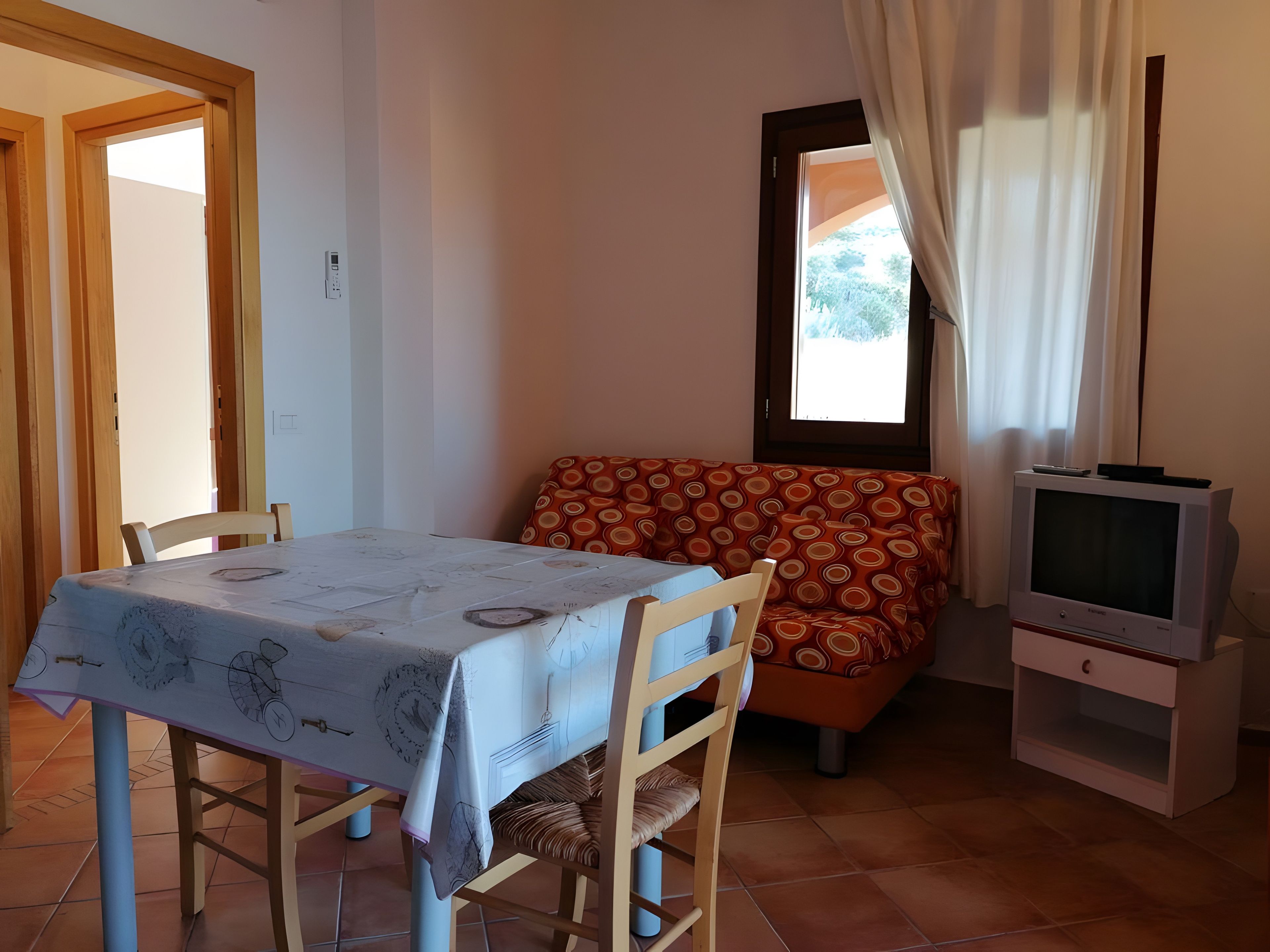 Un coin repas comprenant une table et des chaises, un canapé, un téléviseur et une fenêtre avec des rideaux.