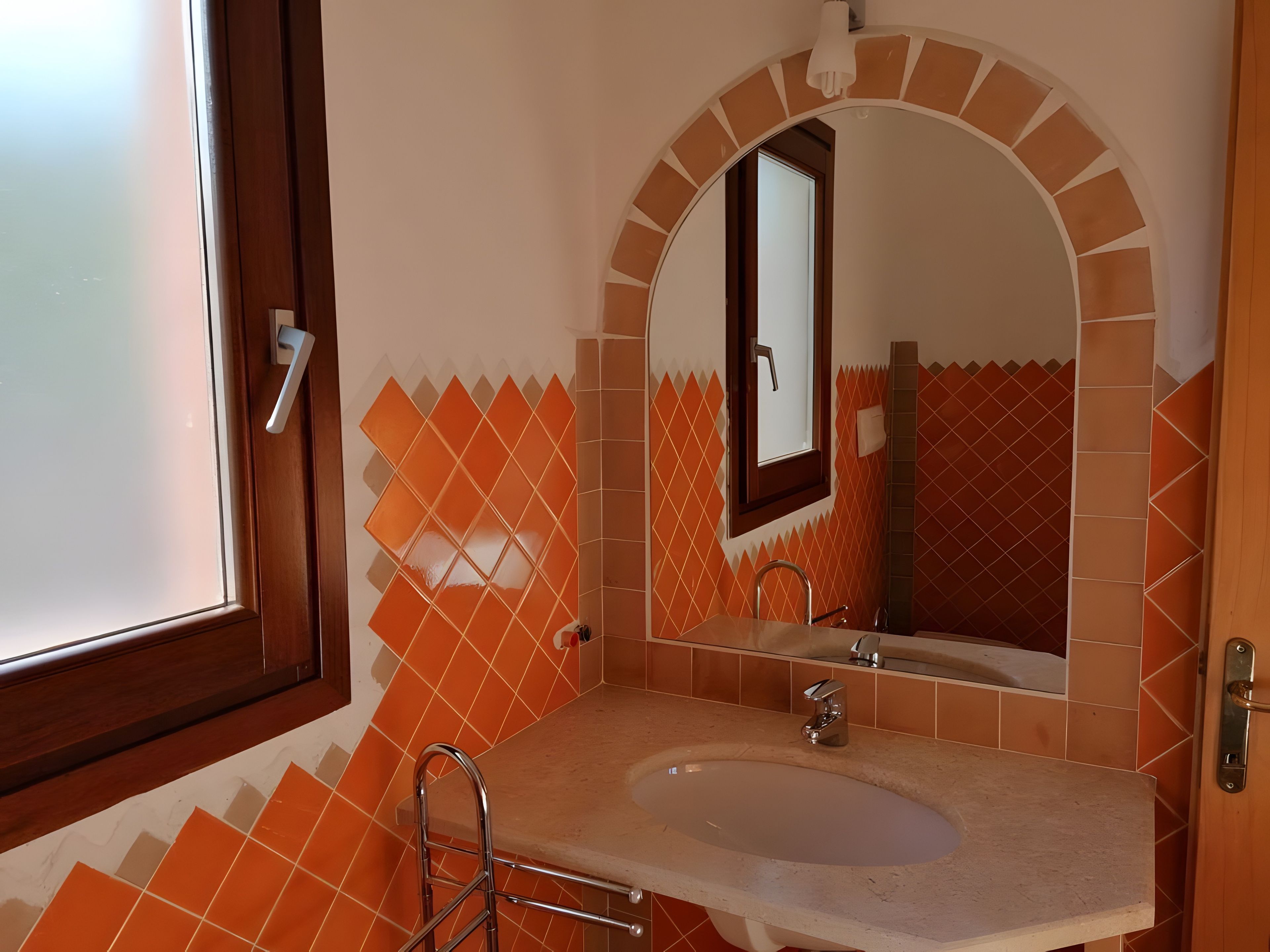 A bathroom with a sink, mirror, and orange-tiled walls.