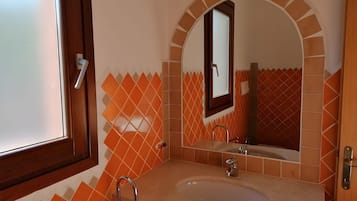 A bathroom with a sink, mirror, and orange-tiled walls.