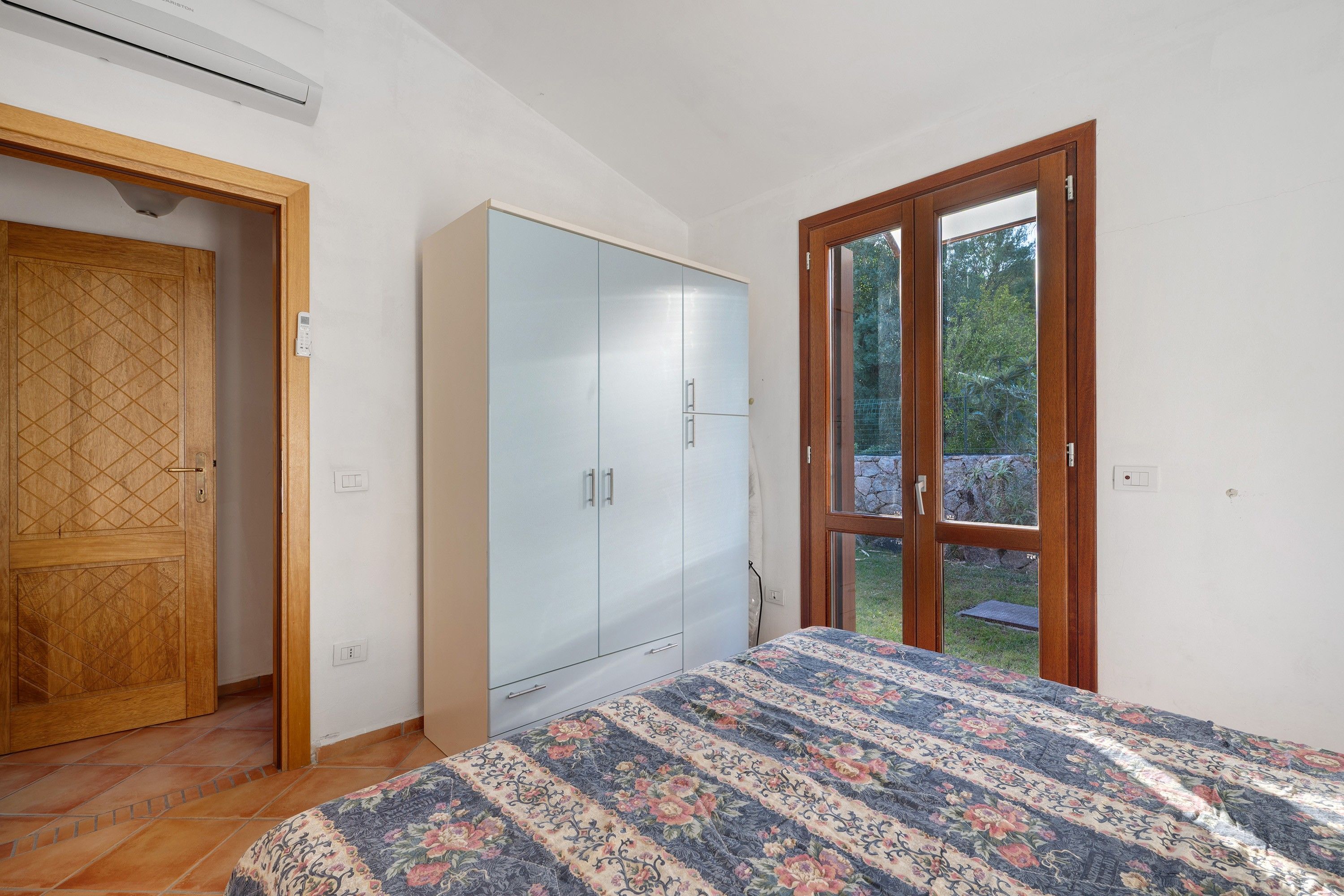 Un dormitorio con cama, armario y puerta que da a un balcón.