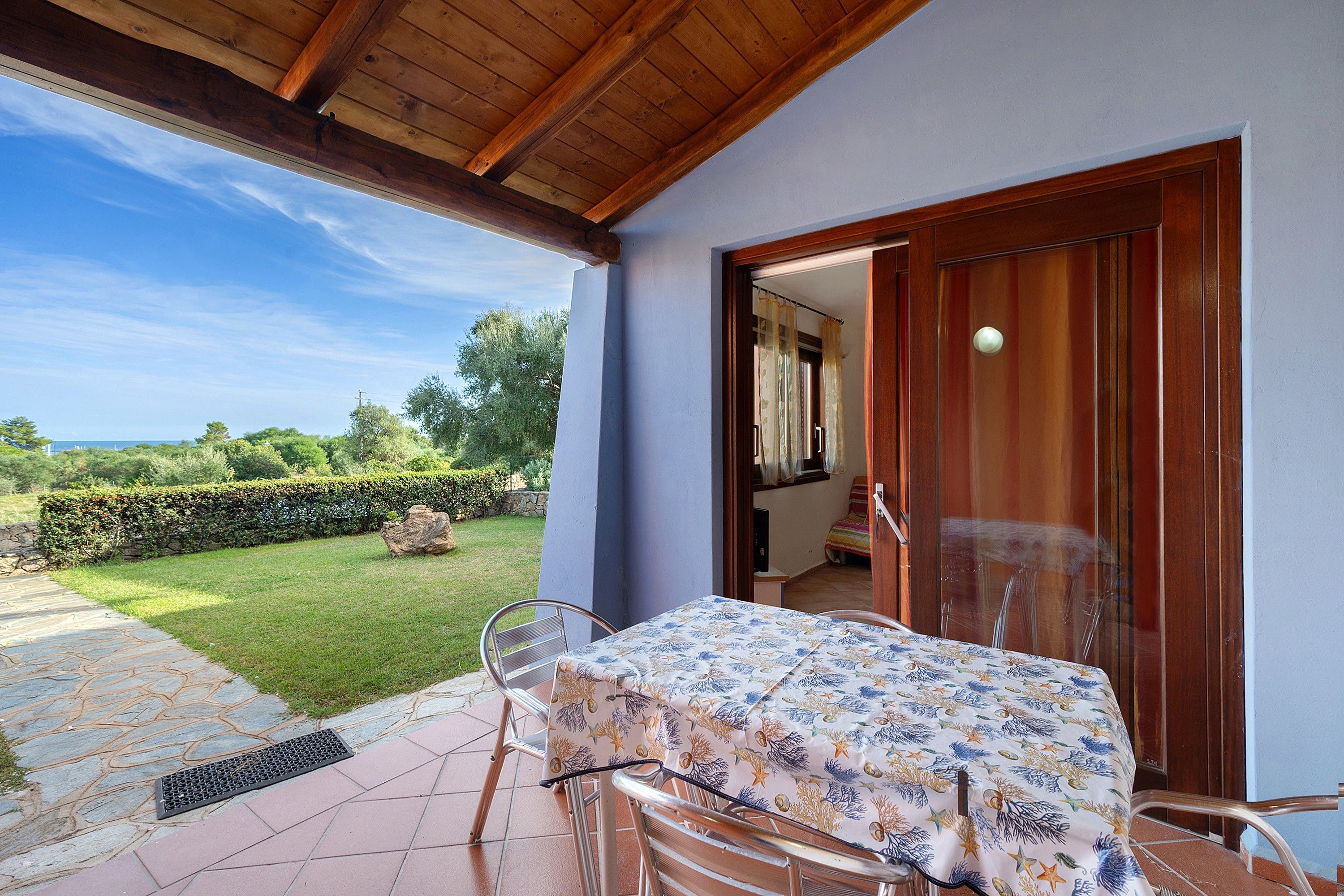 Un patio exterior con mesa y sillas, una puerta de madera y vistas al jardín y al cielo.
