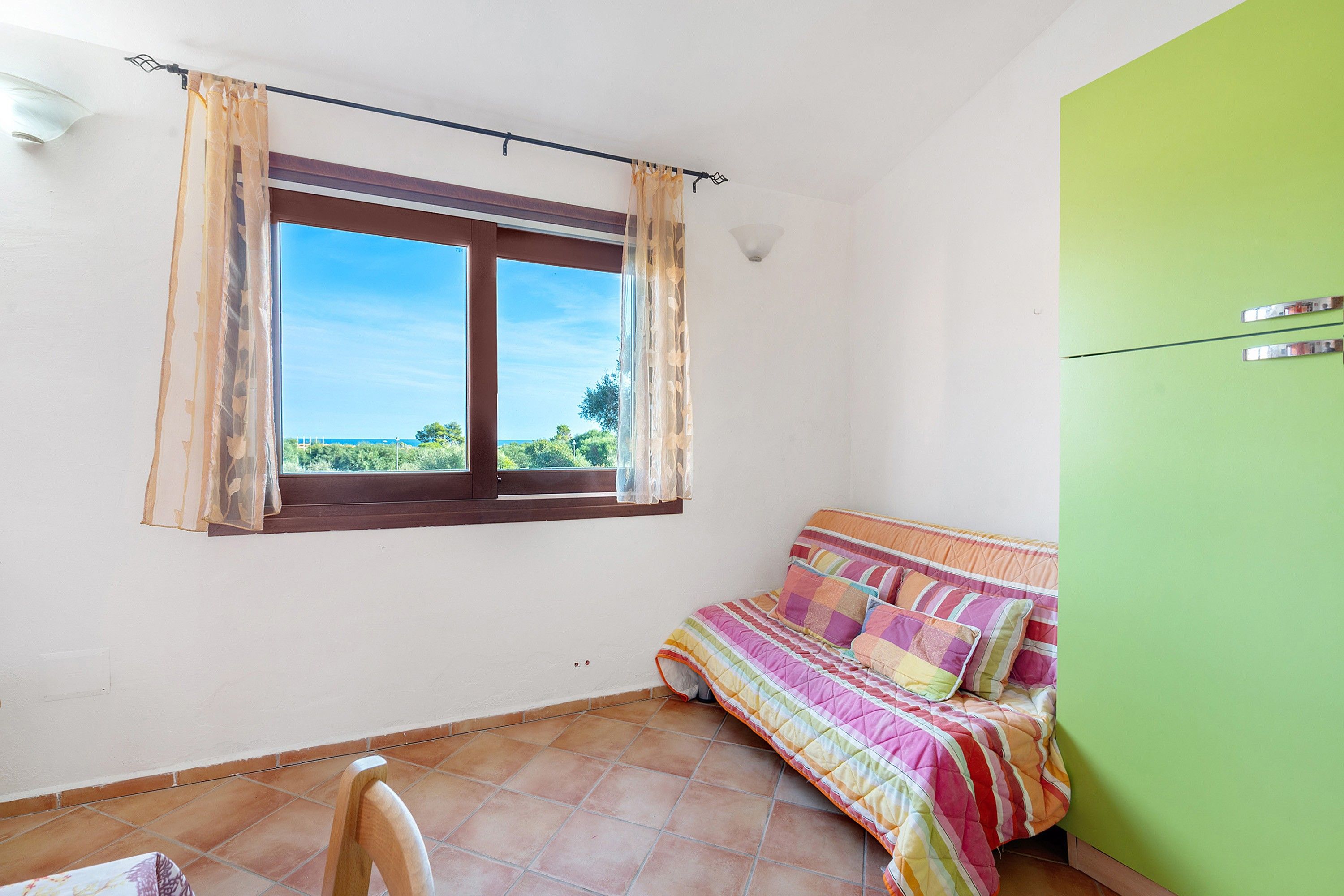 Un dormitorio con cama, ventana con cortinas, pared verde y piso de baldosas.
