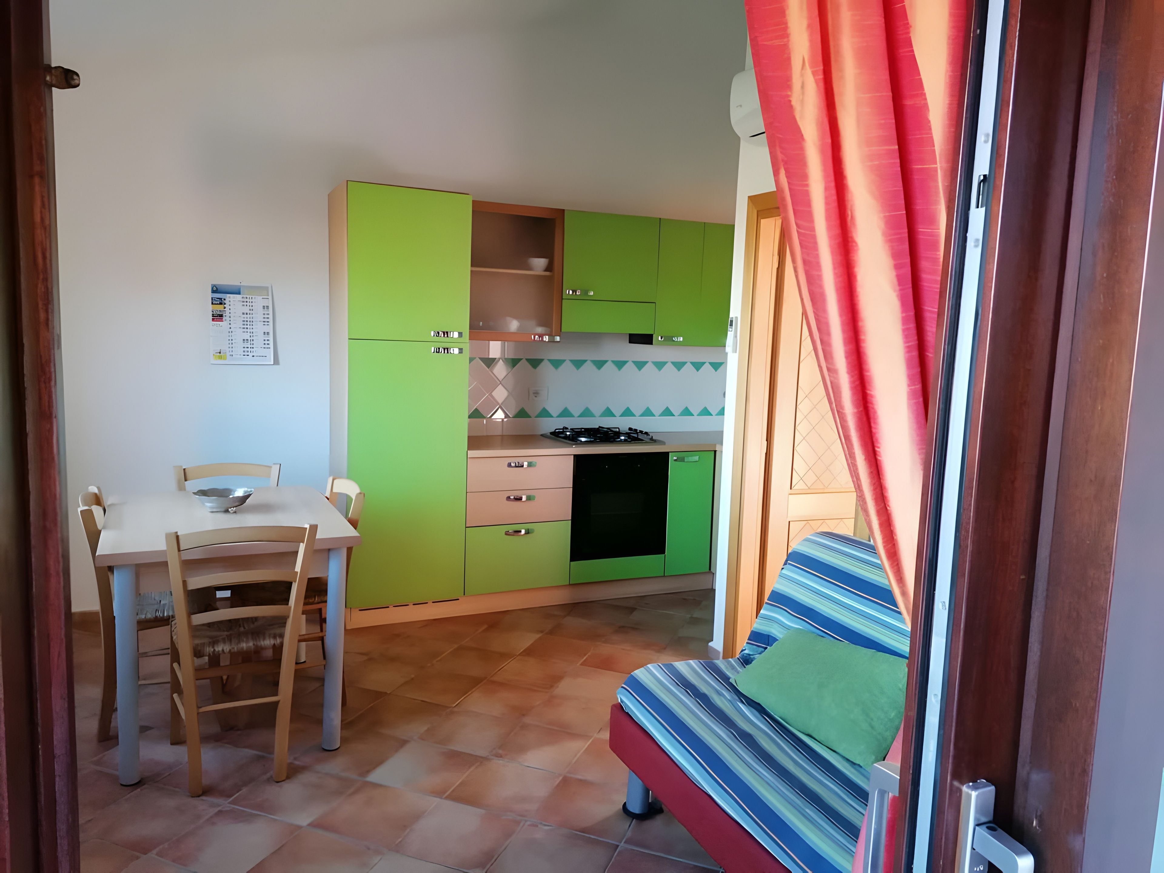 Une cuisine compacte avec des meubles de couleur verte, une table à manger avec des chaises et un coin cuisine.