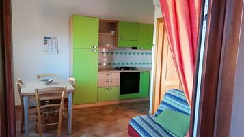 Une cuisine compacte avec des meubles de couleur verte, une table à manger avec des chaises et un coin cuisine.