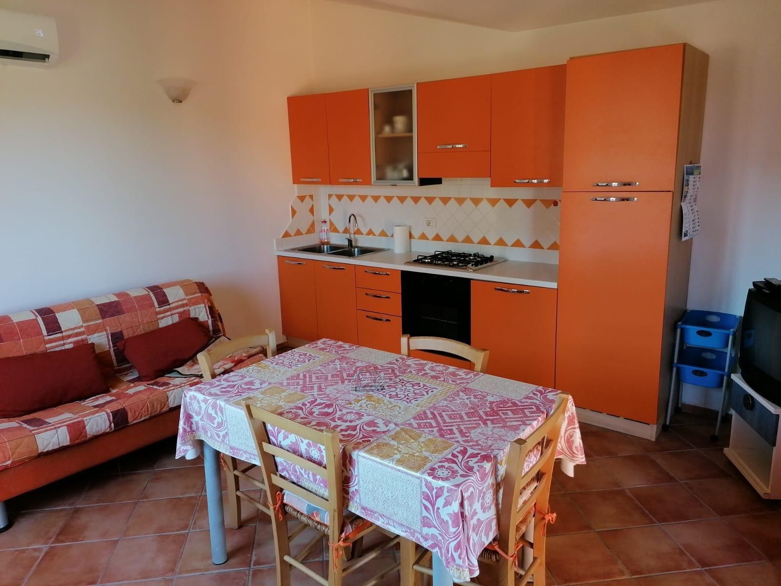 Une cuisine de taille réduite avec des meubles de couleur orange, une cuisinière à gaz et une table à manger avec des chaises.