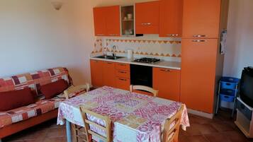 A compact kitchen with orange cabinets, a gas stove, and a dining table with chairs.