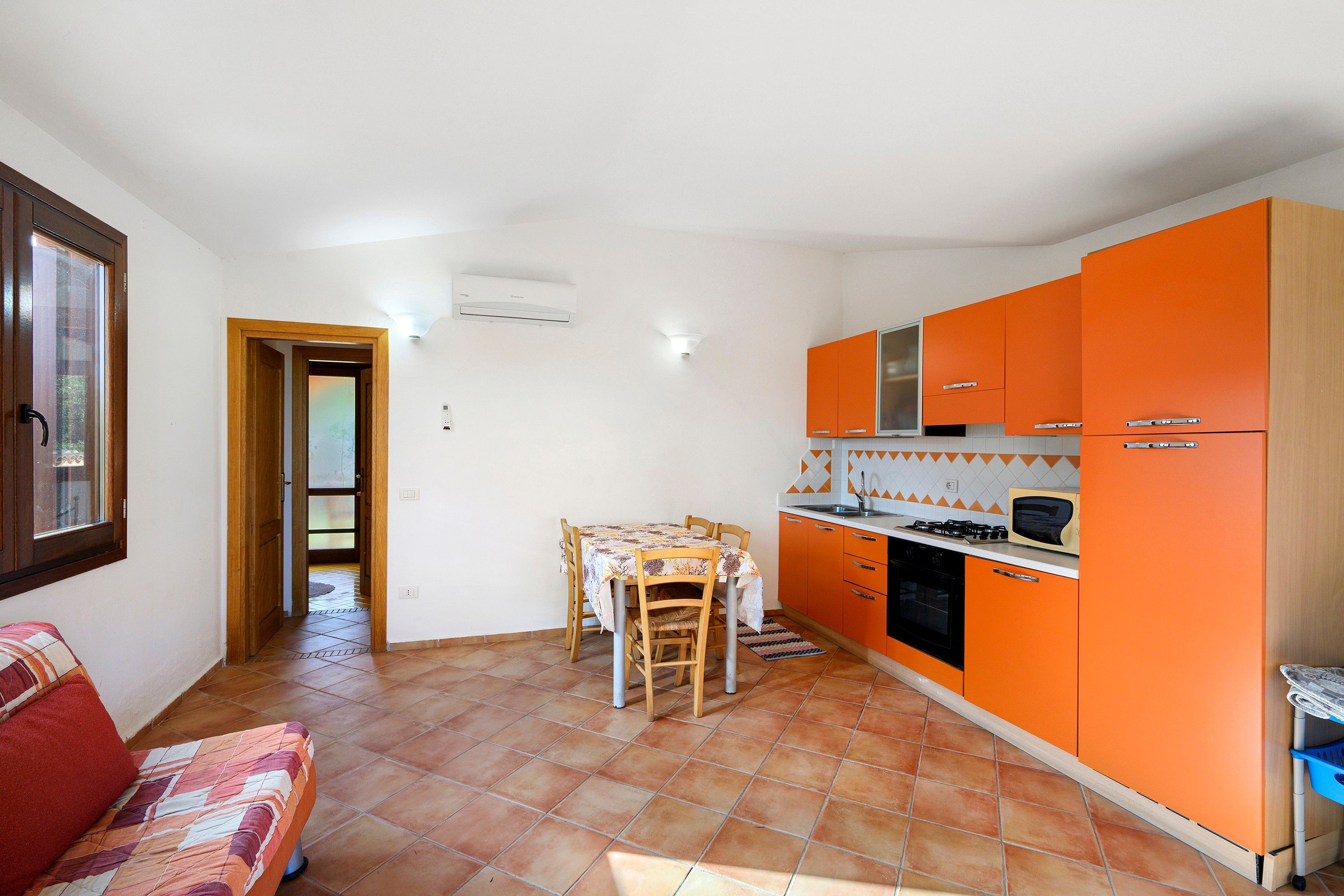 Una cucina compatta con mobili arancioni, un tavolo da pranzo con sedie e un pavimento piastrellato.