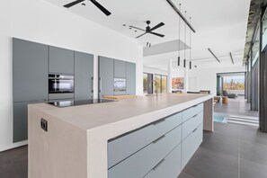 Een moderne keuken met grijze kastjes, een groot eiland en uitzicht op de omgeving.