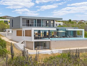 Een modern huis met twee verdiepingen, een zwembad, grote ramen en een trap naar de bovenverdieping.