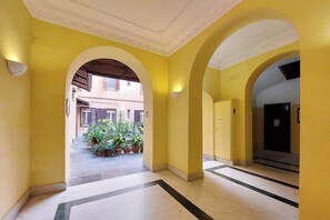 Ein Korridor mit gelben Wänden, einer weißen Decke und einem gefliesten Boden, der zu einem Gebäude mit einer Tür und einem Fenster führt.