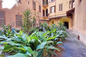 A narrow alley with buildings on either side, featuring balconies with potted plants and a small archway entrance. - Maison Florienne: Charm and Relaxation in the Heart of Rome (Roma)