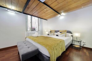 A bedroom with a bed, bedside table, lamp, bench, and a window with a view. - Maison Florienne: Charm and Relaxation in the Heart of Rome (Roma)