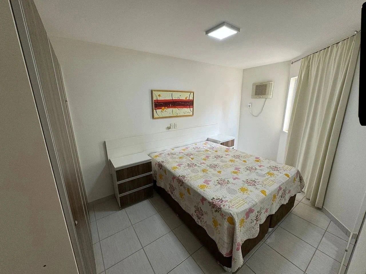 Un dormitorio con cama, mesita de noche, aire acondicionado instalado en la pared y ventana con cortinas.