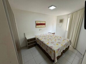 Ein Schlafzimmer mit einem Bett, einem Nachttisch, einer wandmontierten Klimaanlage und einem Fenster mit Vorhängen.