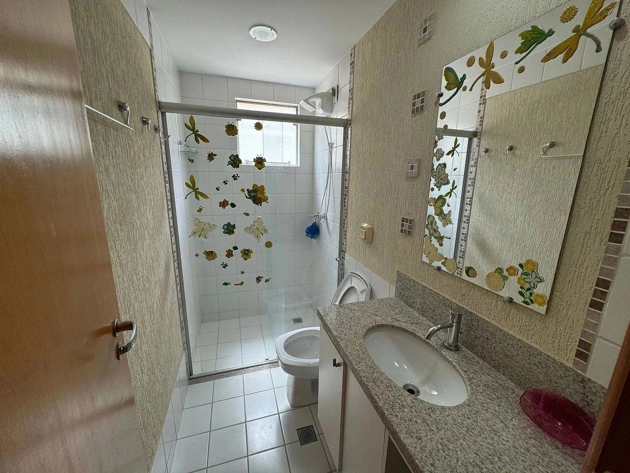 Casa de banho com chuveiro, sanita, lavatório e espelho com decorações florais.