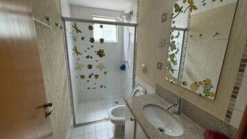 Casa de banho com chuveiro, sanita, lavatório e espelho com decorações florais.