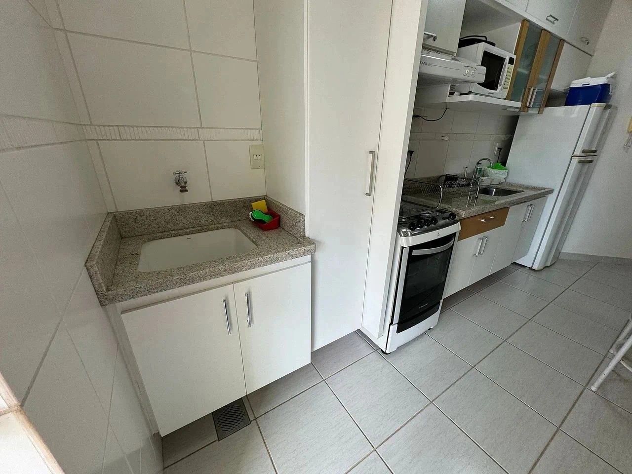Uma cozinha com armários brancos, bancada de granito, fogão e geladeira.