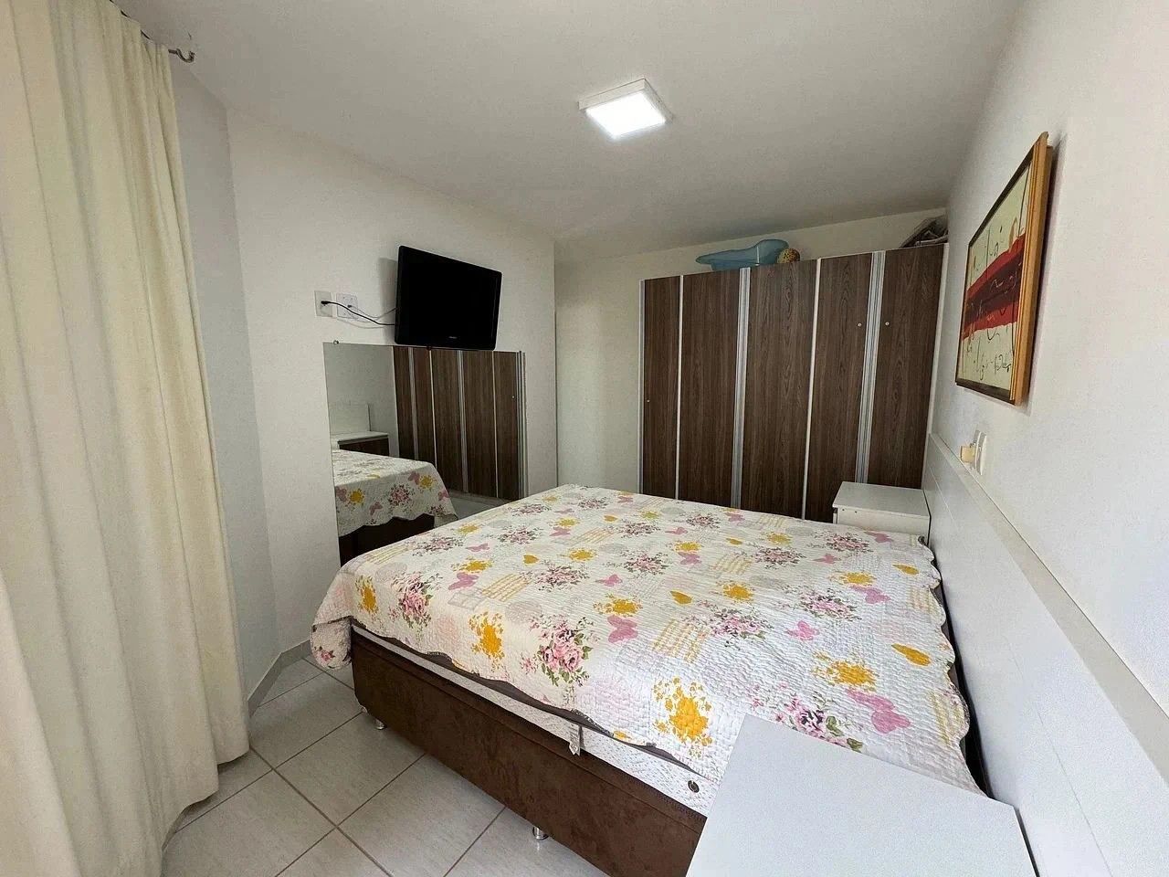 Quarto com cama, televisão, guarda-roupa e um quadro na parede.