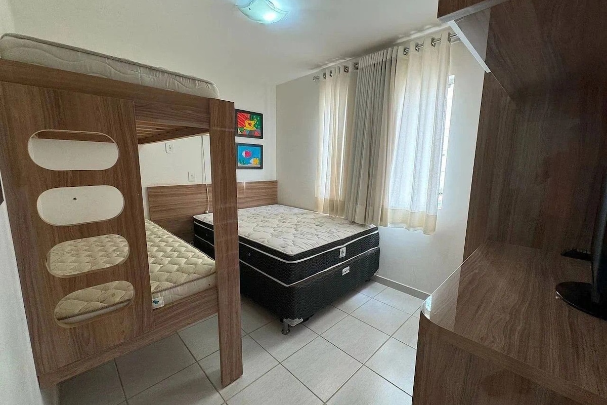 Un dormitorio con una cama litera, una cama individual, un armario y una ventana con cortinas.