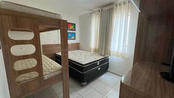 A bedroom with a bunk bed, a single bed, a wardrobe, and a window with curtains.