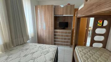 Quarto com cama de solteiro e beliche, guarda-roupa, televisão e escrivaninha.