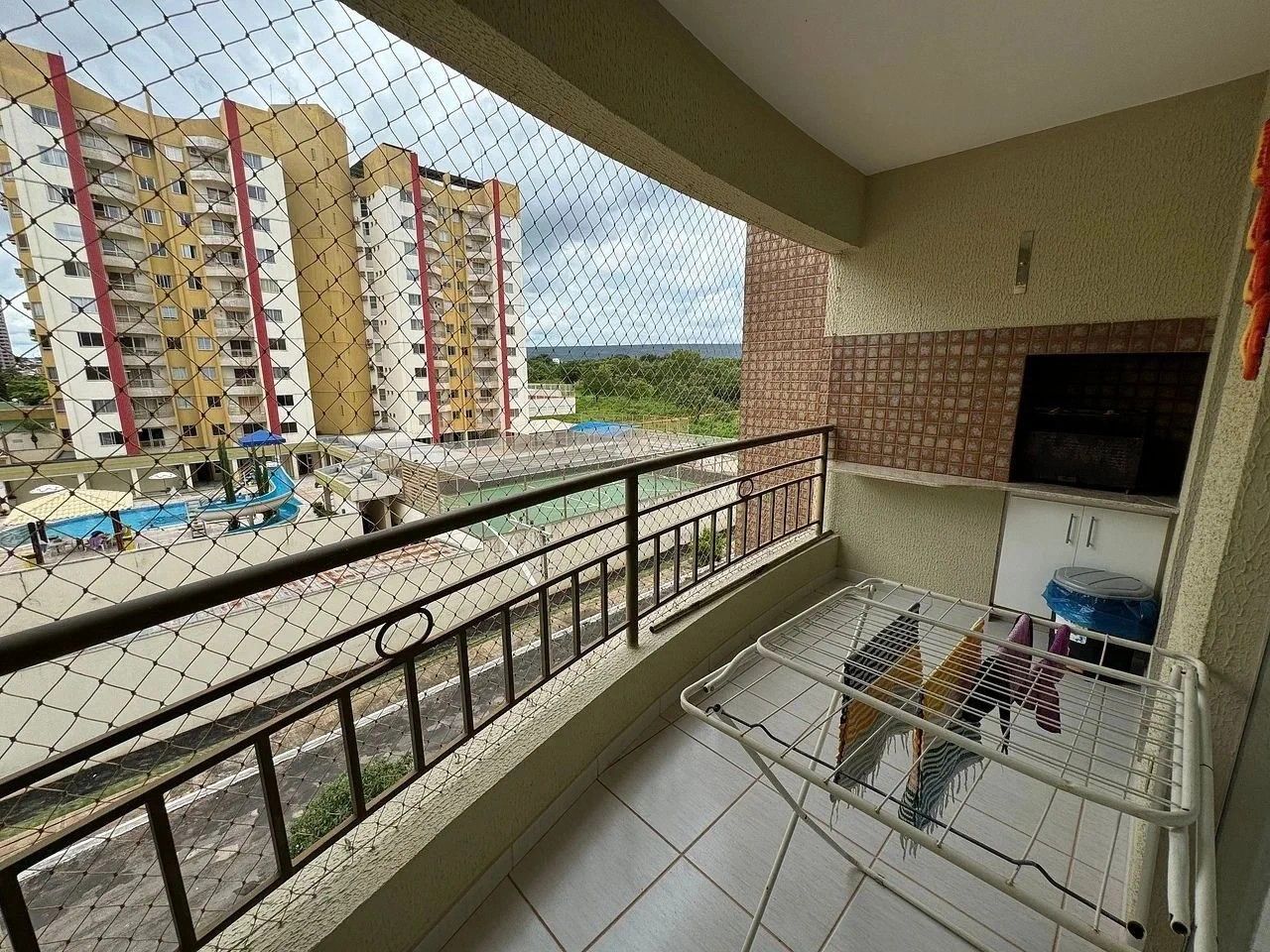 Varanda com vista para edifícios altos, piso ladrilhado e corrimão de metal.