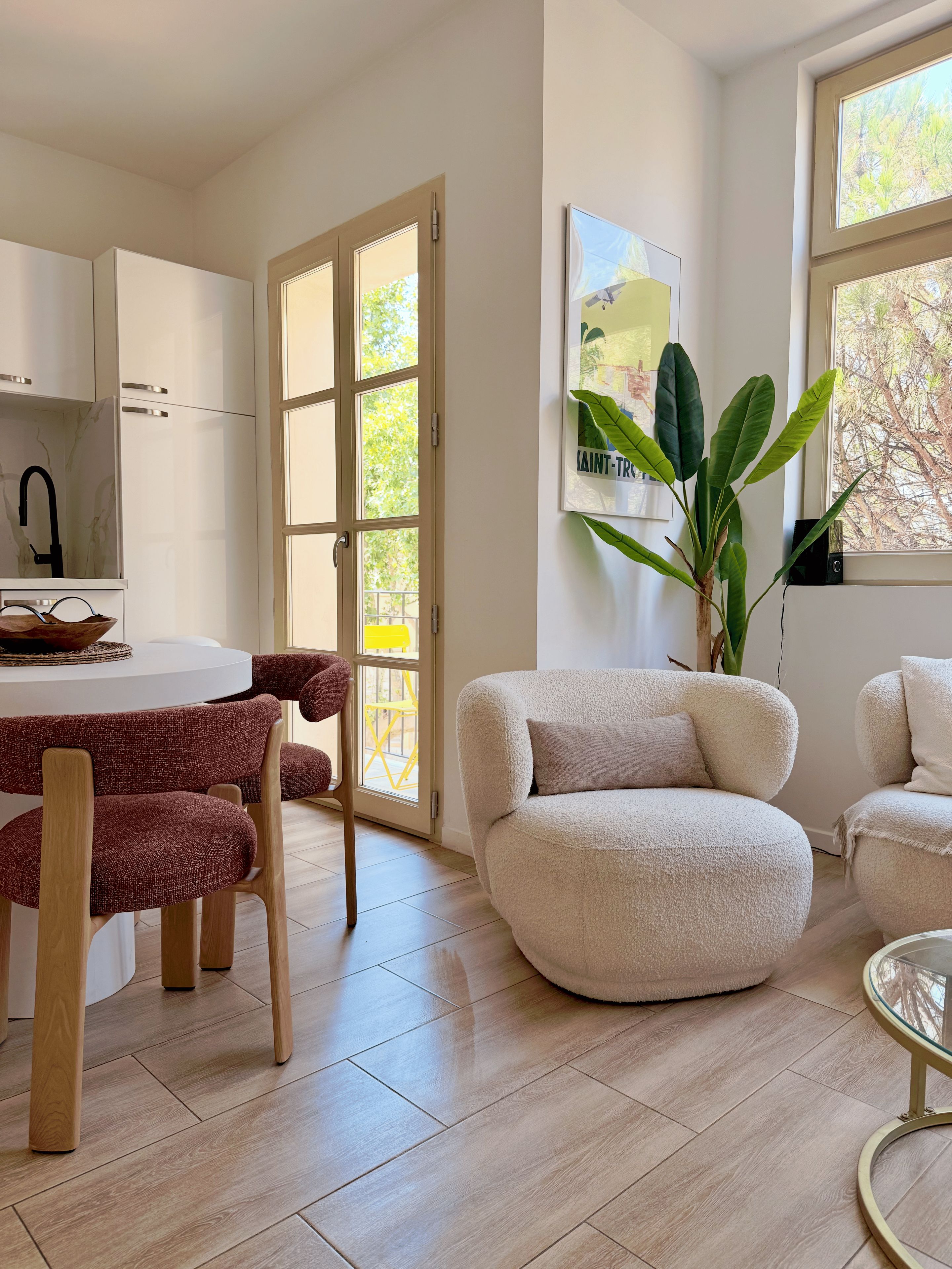 Una cocina moderna con armarios blancos, una mesa de comedor con sillas rojas y un amplio ventanal con vistas a árboles.