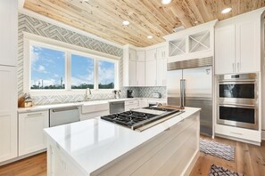 Eine moderne Küche mit weißen Schränken, einer großen Kochinsel mit Gasherd, Backofen und Kühlschrank.