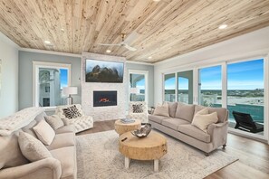 A spacious living room with a fireplace, large windows, and a view of the ocean. - Amberjack | 7BR | Heated Pool & Spa | Sleeps 16 (Inlet Beach)