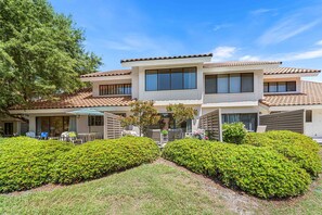 A two-story building with a tiled roof, large windows, and a well-maintained garden with hedges. - Beachwalk Landing 6-Seater Golf Cart | Beach 3–5 Min | Sleeps 8 (Miramar Beach)