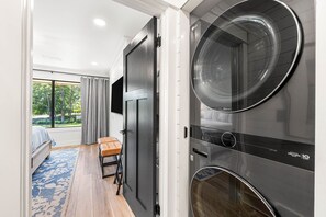 A laundry room with a large washing machine and dryer, a bench, and a bed with a view of the outdoors. - Beachwalk Landing 6-Seater Golf Cart | Beach 3–5 Min | Sleeps 8 (Miramar Beach)