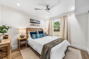 A bedroom with a bed, nightstands, a ceiling fan, a window with curtains, and a view of greenery outside. - Bella Vista | Lakefront 30A | Dock & Kayaks (Seacrest)