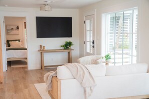 A modern living room with a white sofa, a wooden console table, and a large window with blinds. - Bella Vista | Lakefront 30A | Dock & Kayaks (Seacrest)