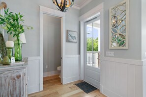 A hallway with a wooden floor, white walls, a door leading to a balcony, and a decorative mirror. - Blue Grouper | Pool | Bikes | Games | 30A (Seagrove Beach)