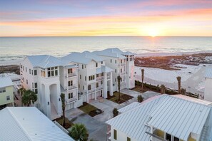 A multi-story hotel with a central courtyard, white exterior, and a view of the ocean at sunset. - Coastal View | Gulf Views | Pool & Hot Tub (Inlet Beach)