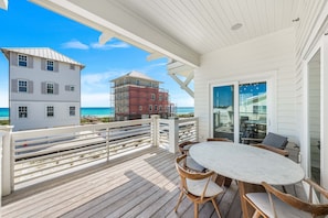 A wooden deck with a table and chairs, overlooking a beach and a building under construction. - Coastal View | Gulf Views | Pool & Hot Tub (Inlet Beach)