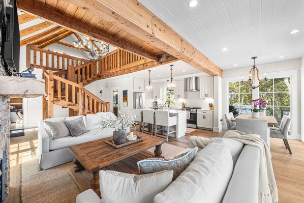 A spacious living area with a wooden staircase, a kitchen with white cabinets, and a dining area with a view of trees. - Coastal Vista 30A | Private Dock | 2 Homes (Seacrest)