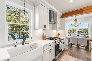 A modern kitchen with white cabinetry, a gas stove, and a large window overlooking a lake. - Coastal Vista 30A | Private Dock | 2 Homes (Seacrest)