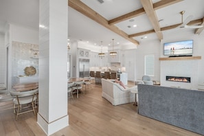 A spacious living area with a fireplace, a dining area with a wooden table and chairs, and a kitchen in the background. - Coral Cay | Pool, Hot Tub & Elevator | Beach Getaway (Inlet Beach)