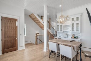 Eine geräumige Küche mit einem Holzespeisetisch und Stühlen, einer Treppe mit Holzgeländern und weißen Schränken mit einer Rückwand aus Bienenkorbmosaik.