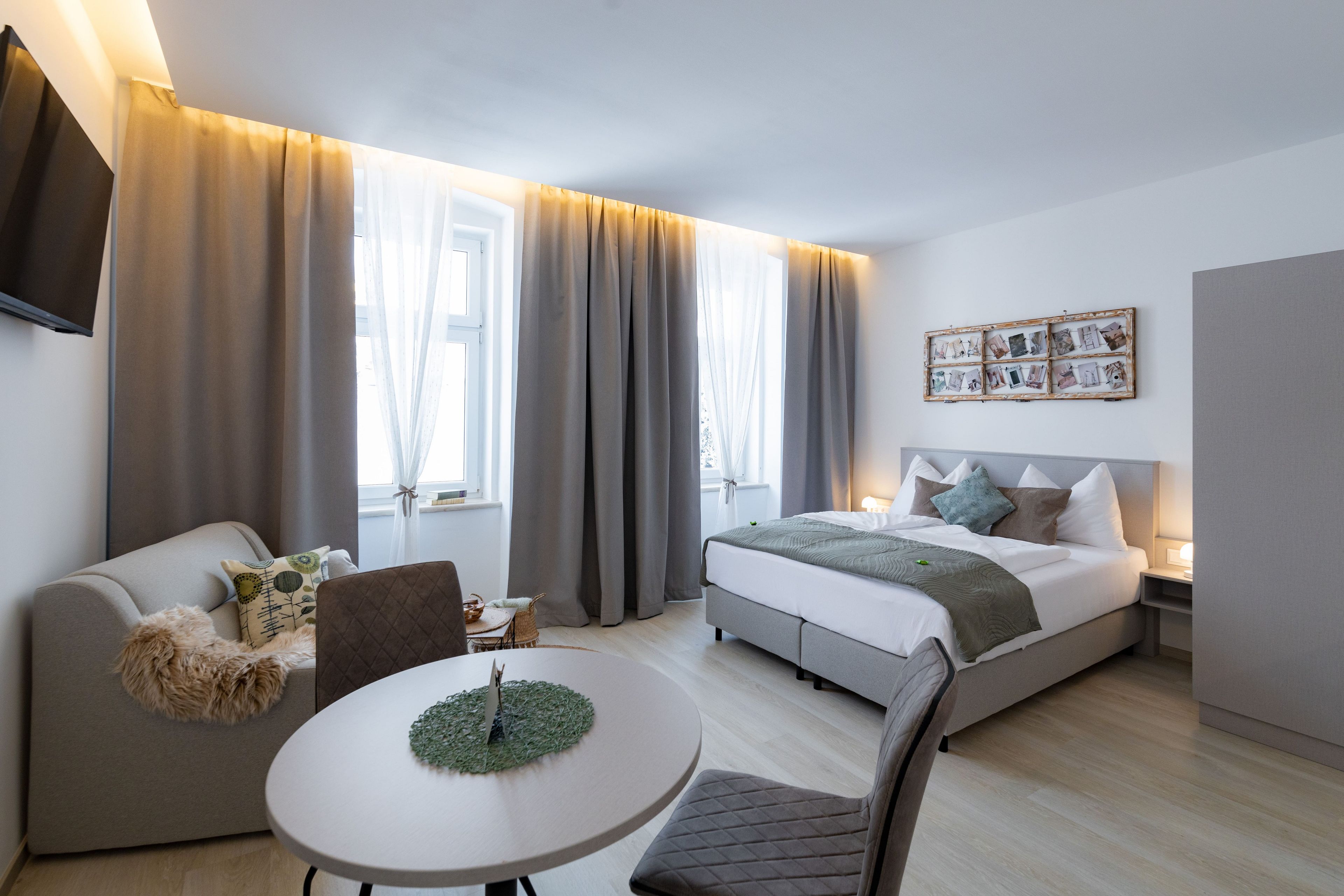 Ein modernes Hotelzimmer mit Bett, Sofa, Esstisch und Fernseher.